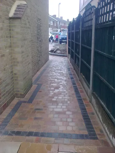 a narrow brick street with green gated buildings in the background