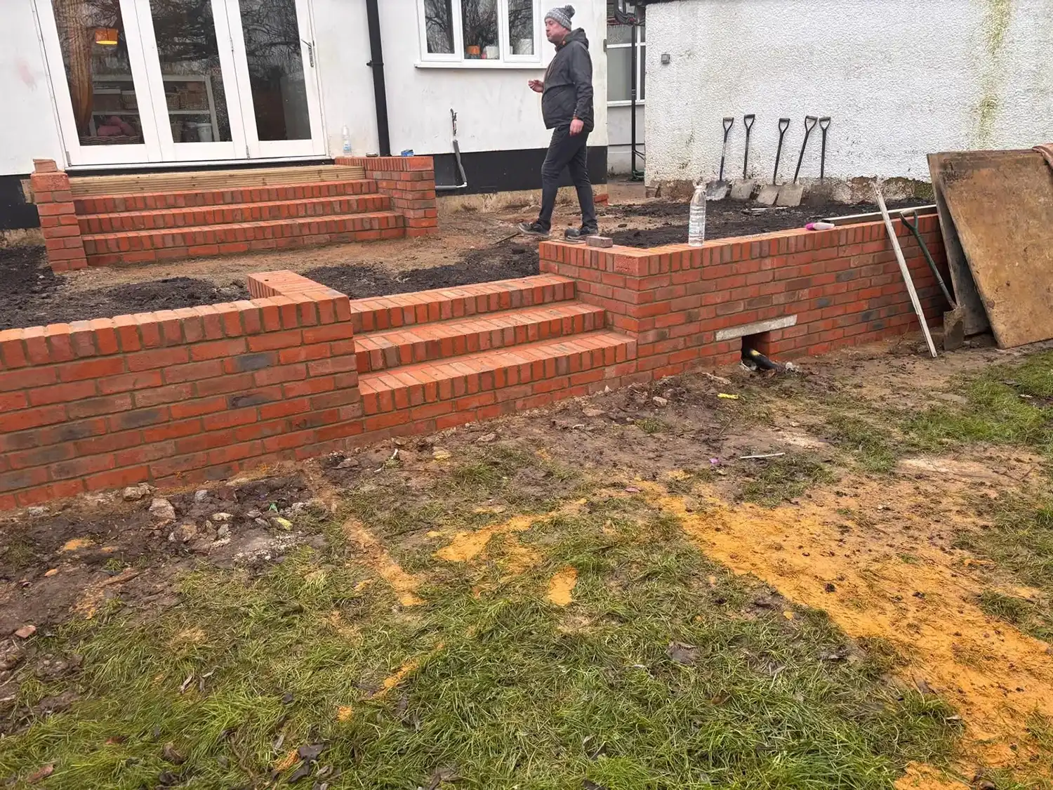 A man walking past a brick wall in a yard.