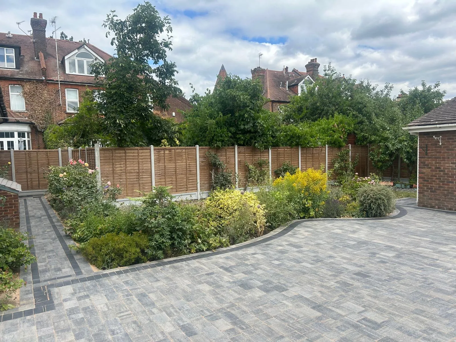 A brick paved driveway with a wooden fence in the background.