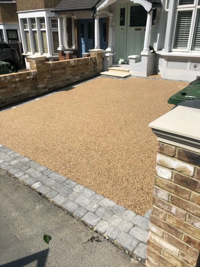 a driveway with a gravel walkway and a brick wall